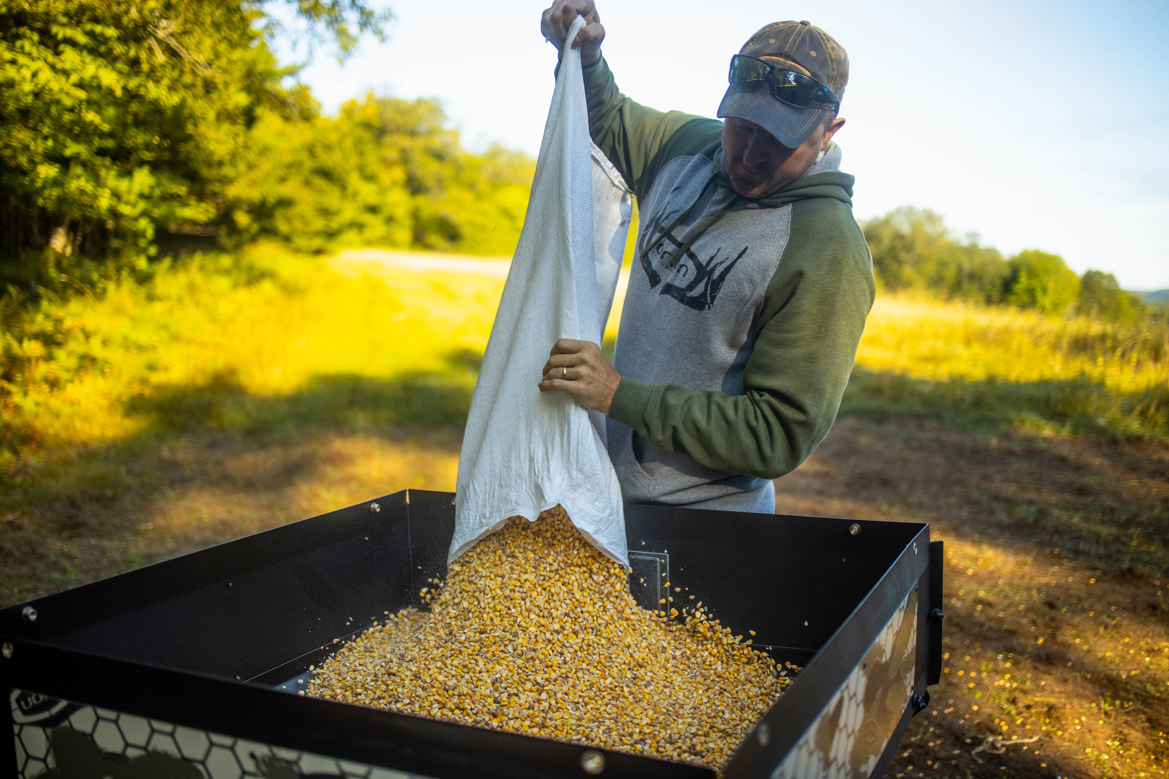 man pouring a bag of corn into an Orion 450lbs modular stand and fill deer feeder in an open field